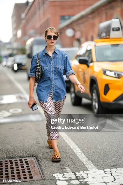 Guest wears black sunglasses, a blue denim shirt from Levis, a beige and blue Dior Oblique Jacquard Saddle shoulder bag from Dior, a gold bracelet,...