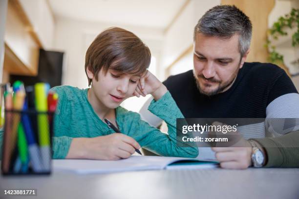 preadolescent boy sitting at home and doing homework with his father - man reliable learning stock pictures, royalty-free photos & images