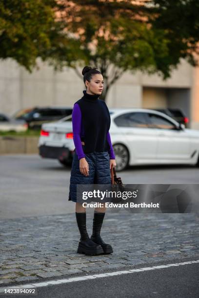 Guest wears silver earrings, a black turtleneck / ribbed wool / breastplate pullover, a neon purple long sleeves wool pullover, black quilted shorts,...
