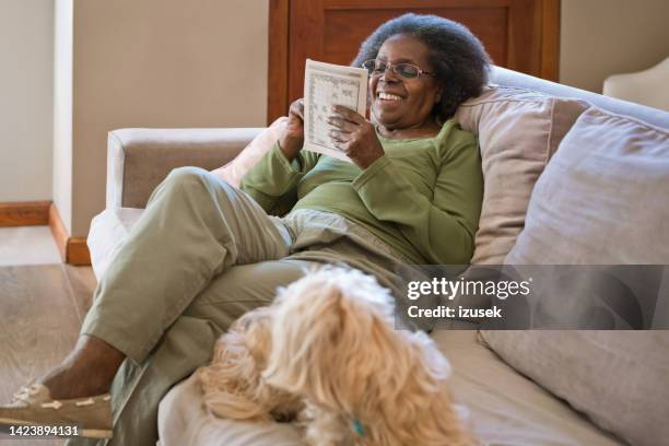 smiling elderly woman reading book by dog at home - one animal stock pictures, royalty-free photos & images