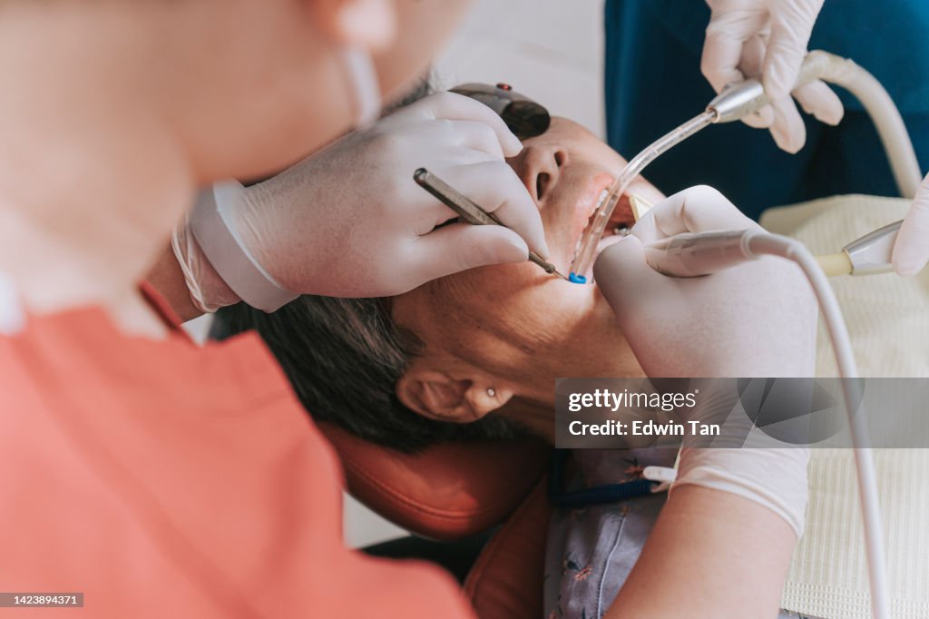 Dentista de cerca reparando la boca del diente de la paciente paciente mayor abierta con la enfermera sosteniendo el tubo de succión