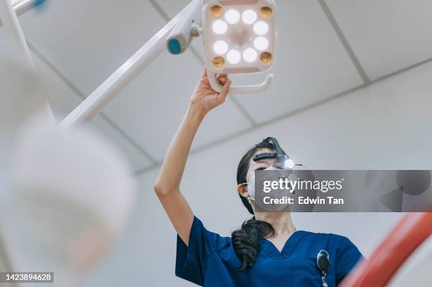 dentista asiática china con lupas ajustando la luz quirúrgica mirando desde arriba al paciente - asian ceiling fotografías e imágenes de stock