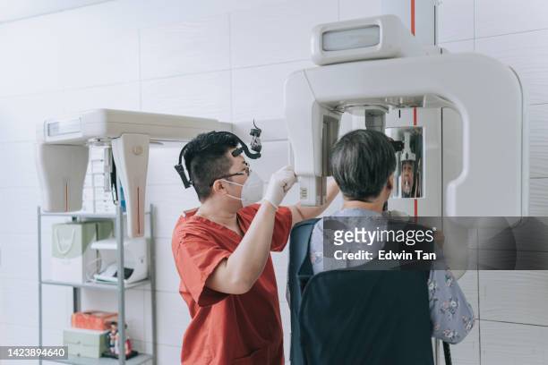 dentista masculino chino asiático capturando imagen de rayos x médicos con paciente mayor en sala de rayos x - odontología cosmética fotografías e imágenes de stock