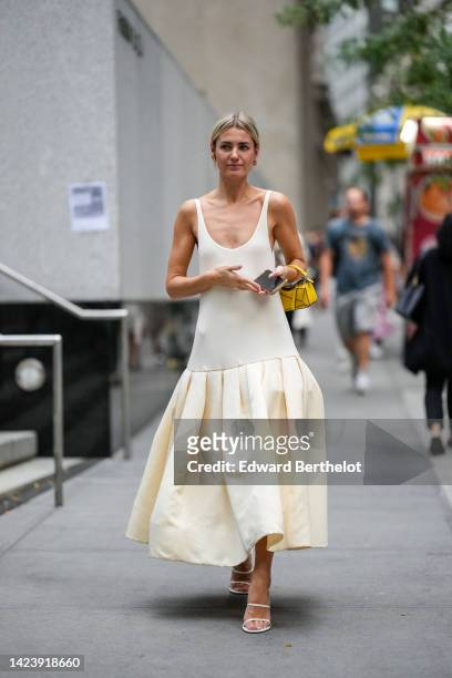 Guest wears gold earrings, a white latte V-neck / tank-top long ruffled dress, a yellow shiny leather micro Puzzle handbag from Loewe, white strappy...