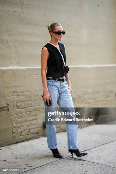 Guest wears black sunglasses, a black V-neck / sleeveless gilet, a black shiny leather with white large pearls crossbody strap small clutch from...