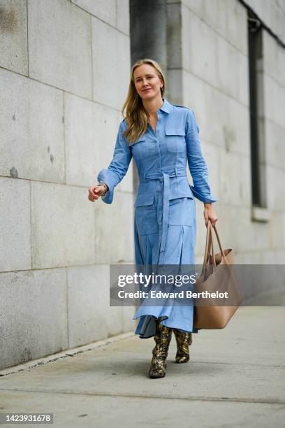 Guest wears gold earrings, a blue long sleeves / belted / long dress, a brown shiny leather large handbag, beige and black shiny leather snake print...