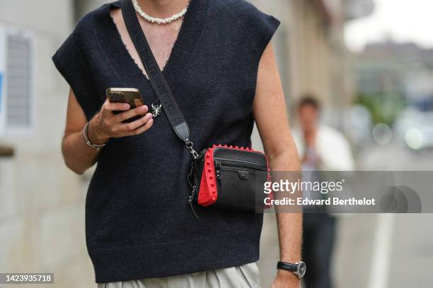 Guest wears a white pearls necklace, a black V-neck / wool / sleeveless pullover, a black and red shiny leather nailed / studded crossbody bag from...