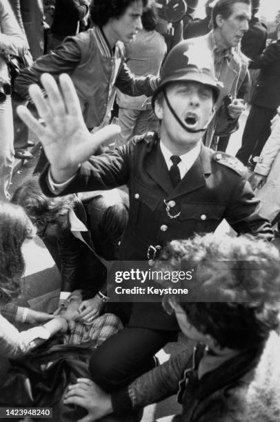 An unspecified police officer attempts to maintain calm as unspecified people tend to an injured man on the ground, after members of the National...