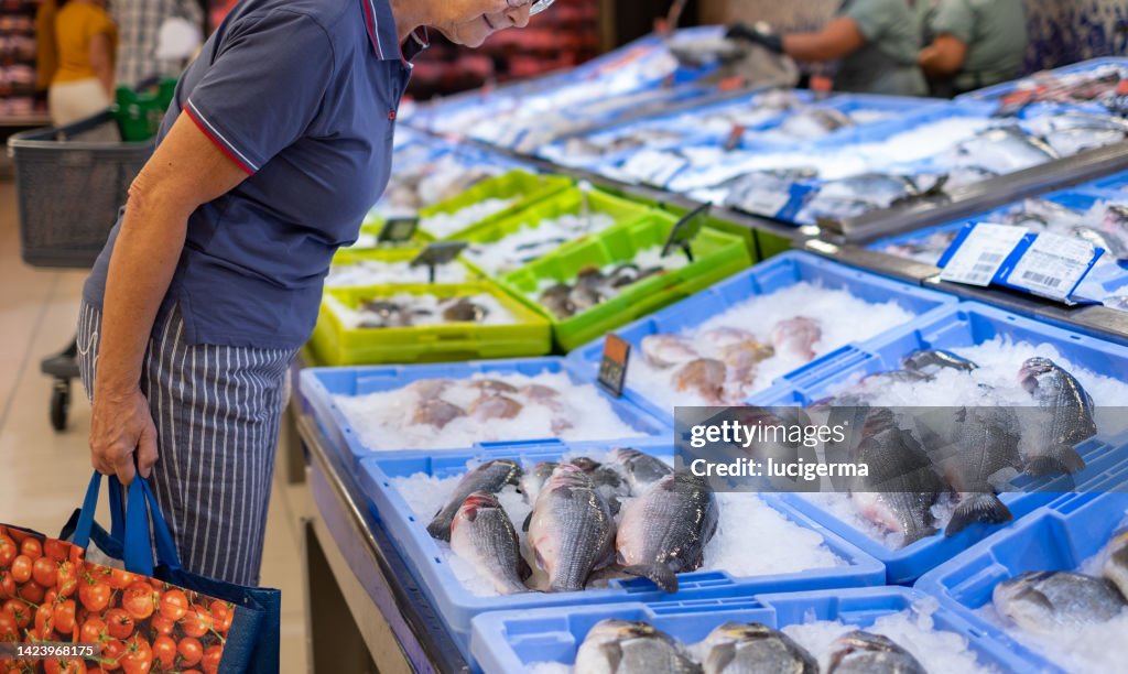 Senior caucasian woman shopping for fresh seafood at the supermarket retail store