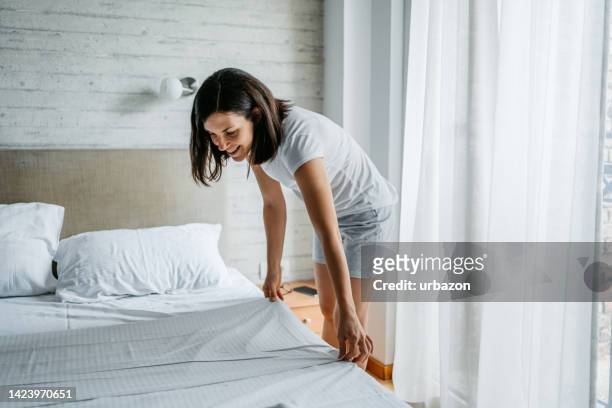 young woman making the bed in the morning - bedsheets stockfoto's en -beelden