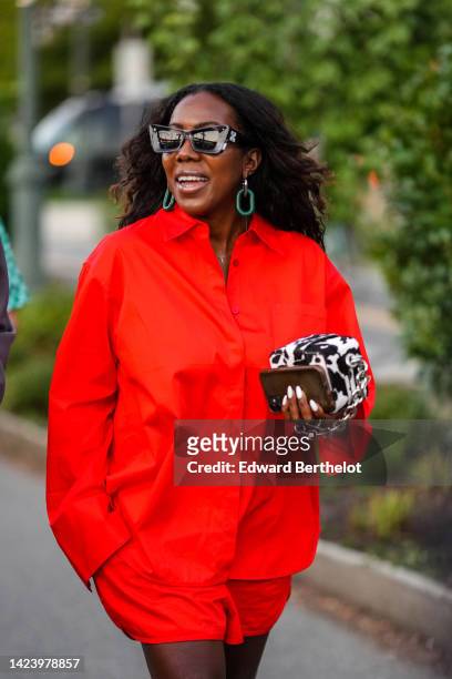 Guest wears black sunglasses from Off-White, green earrings, a gold necklace, a neon red shirt, matching neon red shorts, a black and white cow print...