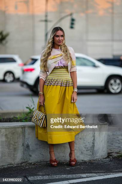 Guest wears earrings, a pale purple blouse, a pale purple and yellow tie and dye print pattern knot wool cropped pullover, a yellow and purple...
