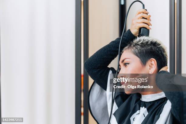 new haircut. mature blond and black haired woman shaving hair with electric razor, trimmer. copy space - shave barber stock pictures, royalty-free photos & images