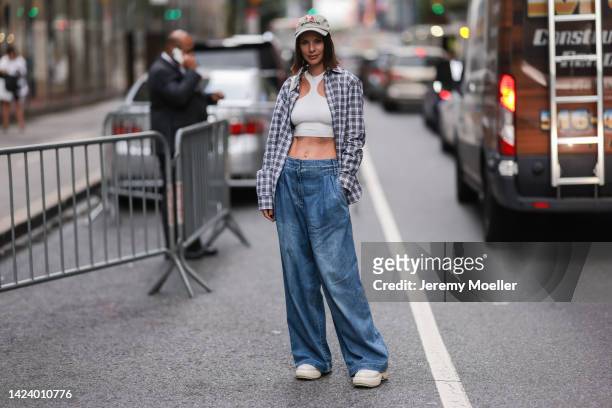 Fashion week guest seen wearing beige blue embroidered pattern cap, a white halter-neck / cut-out shoulder cropped top, a black and white checkered...