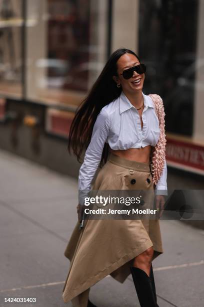 Fashion week guest seen wearing a white cropped blouse, beige skirt with trench coat look, black high waist boots outside Brandon Maxwell during New...