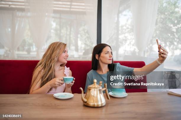 mother and adult daughter met in a cafe, using smartphone, video call to family - mom buying milk photos et images de collection