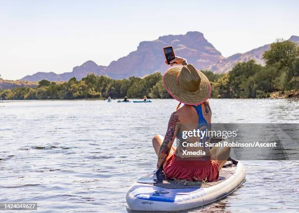 young woman takes photo while floating down river on sup - glen canyon stock pictures, royalty-free photos & images