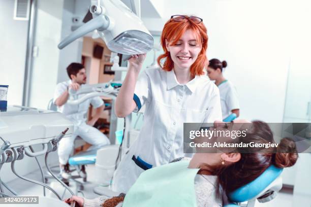 dentista femenina segura y sonriente que revisa la cavidad bucal del paciente con luz - radiologia dental fotografías e imágenes de stock