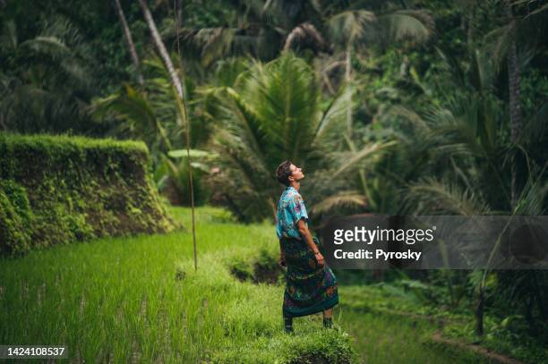 a young man stands on a beautiful rice terrace in ubud, bali, indonesia - tegallalang stock pictures, royalty-free photos & images