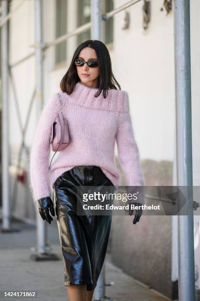 Mary Leest wears black sunglasses, a pale purple wool shoulder-off / long sleeves / oversized pullover, black shiny varnished leather gloves, a matte...
