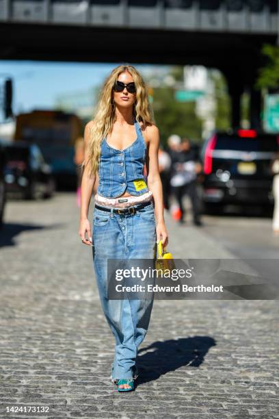 Emili Sindlev wears black sunglasses, gold large earrings, a blue denim V-neck / buttoned / tank-top from Ganni, a gold silk bower from Miu Miu, a...