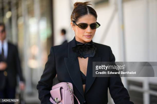 Thassia Naves wears black sunglasses, black hair clips, diamonds earrings, a black flower large necklace, a black asymmetric cropped jacket, a pale...