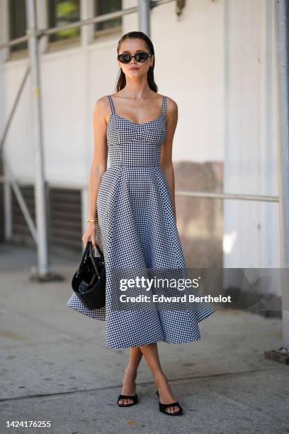 Guest wears a black and white checkered print pattern V-neck / tank-top / midi dress, a black shiny leather handbag, black suede heels mules, black...