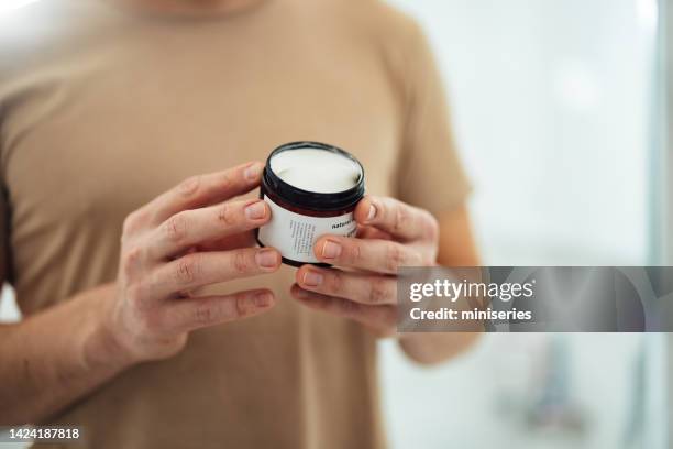 hombre anónimo sosteniendo crema facial en el baño (espacio de copia) - hombre crema facial fotografías e imágenes de stock