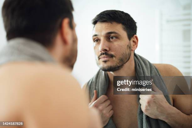 portrait of a handsome man checking his appearance in a bathroom mirror in the morning at home - male looking content stock pictures, royalty-free photos & images
