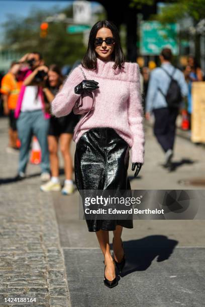 Mary Leest wears black sunglasses, a pale purple wool shoulder-off / long sleeves / oversized pullover, black shiny varnished leather gloves, a matte...