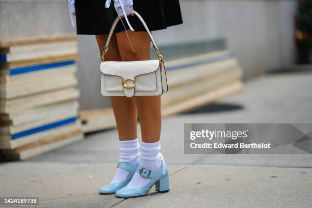 Guest wears a black pleated short skirt, a white shiny leather handbag from Coach, white socks, pale blue shiny varnished leather block heels...