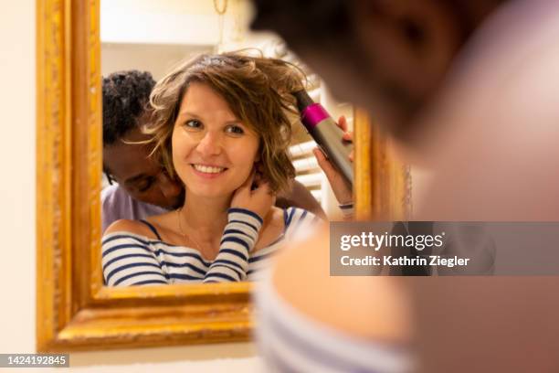 woman curling her hair in front of bathroom mirror, boyfriend kissing her on the neck - couple and kiss and bathroom 個照片及圖片檔