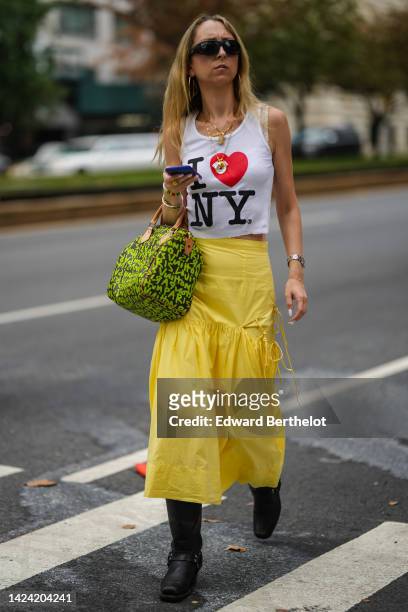 Guest wears a white with black and red "I Love NY" slogan print pattern tank-top, a yellow ruffled midi skirt, a black with green inscriptions print...