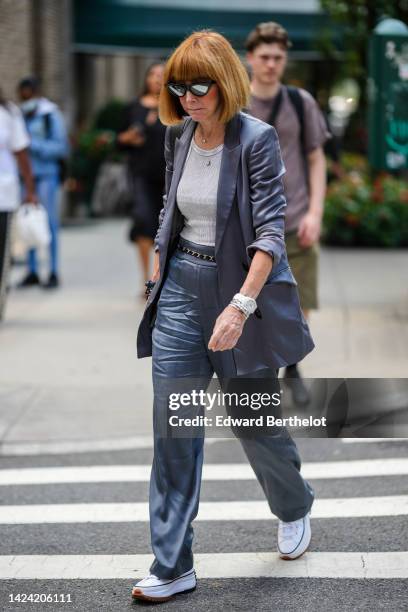 Guest wears black sunglasses, a white t-shirt, a shiny gray long blazer jacket, matching shiny gray suit pants, a black shiny leather and gold chain...