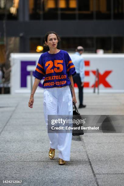 Guest wears a royal navy blue with neon orange print pattern sport t-shirt, white large pants, a black handbag, gold shiny varnished leather shoes ,...