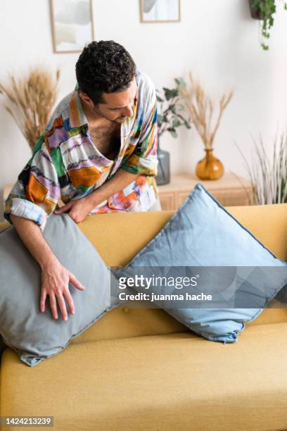 man arranging cushions on the sofa - cushion stockfoto's en -beelden