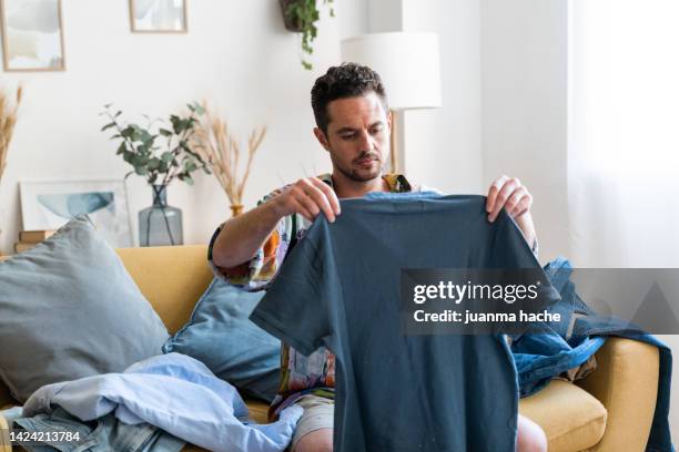 man sorting his clothes sitting on a sofa. - washing up stock-fotos und bilder