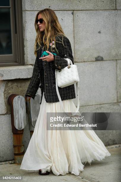Guest wears black sunglasses, a black with gold details tweed jacket, a white latte tulle pleated / accordion long skirt, a white shiny leather Lady...