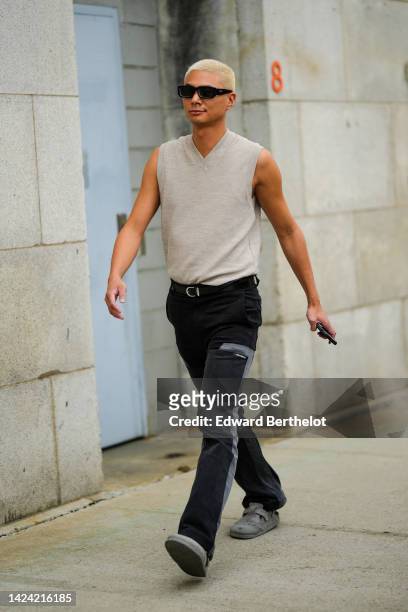 Guest wears black sunglasses, a beige sleeveless wool pullover, black and gray yok large pants, gray suede mules , outside Gabriela Hearst, during...