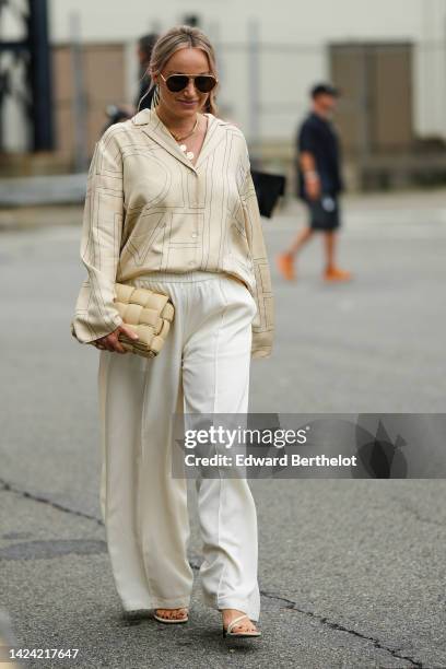 Guest wears black aviator sunglasses, gold necklaces , a gold with black print pattern silk shirt, a beige matte leather puffy Cassette handbag from...