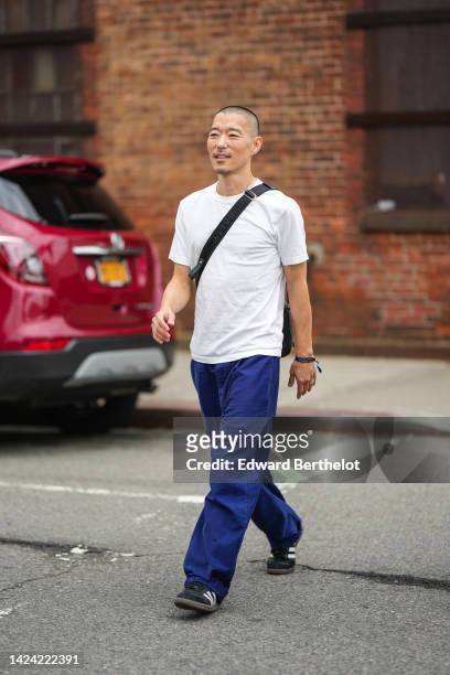 Guest wears a white t-shirt, a black crossbody bag, navy blue large pants, black suede with white leather sneakers from Adidas, outside Gabriela...