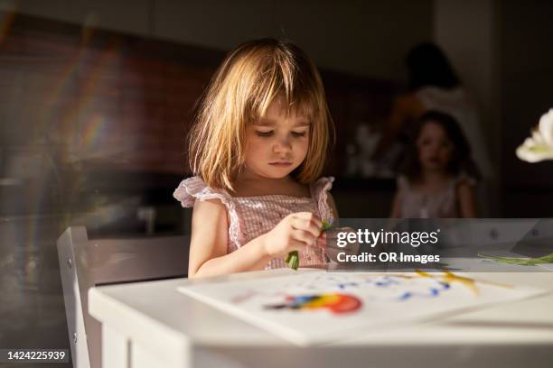 serious girl sitting at table at home with family in background - sad girl drawing photos et images de collection