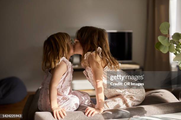 two sisters kissing on sofa in sunlight - kiss sisters stock pictures, royalty-free photos & images