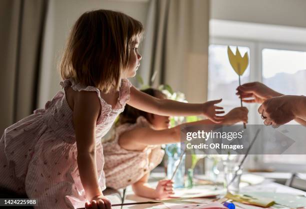 girl handing over paper flower to mother at home - paper flower stock-fotos und bilder