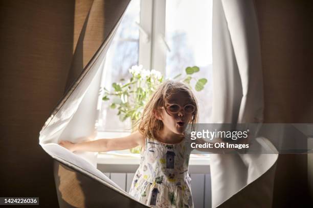 playful girl opening curtain at the window at home - open day 4 stock pictures, royalty-free photos & images