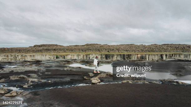 teenage boy walking on muddy cliff edge wearing a head net at a river - dettifoss waterfall stock pictures, royalty-free photos & images