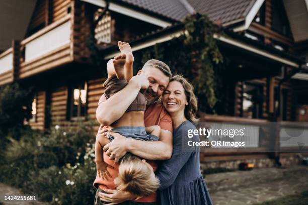 happy father with wife holding son upside down in front of house - gartenhaus stock-fotos und bilder