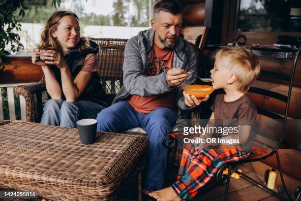 father feeding son with porridge on porch - boy eating cereal stock pictures, royalty-free photos & images