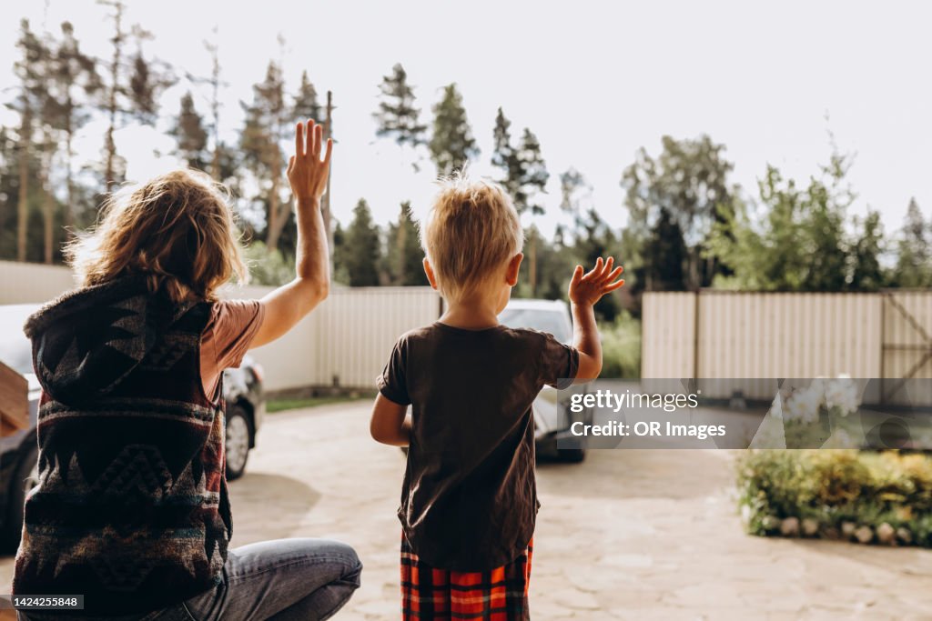 Rear view of mother and son waving on driveway