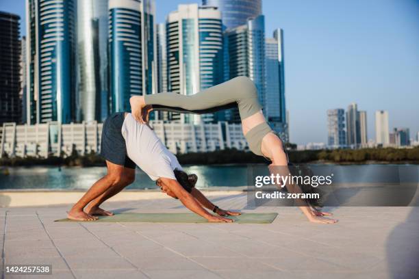 mann und frau praktizieren yoga zu zweit auf dem pier in abu dhabi - abu dhabi beach stock-fotos und bilder